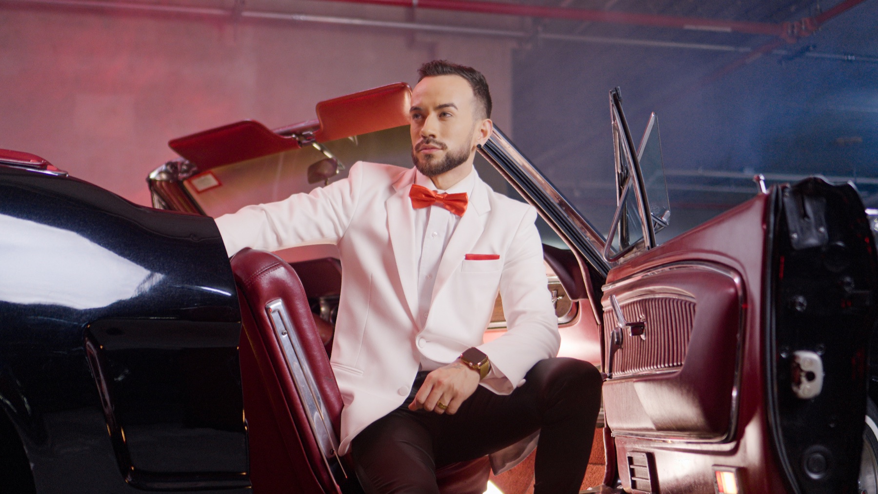 Retrato de un hombre con traje blanco junto a un automóvil clásico